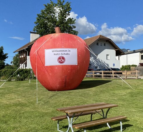 Auf einer Wiese steht ein großer, roter Apfel. Es ist ein aufblasbarer Werbeträger.