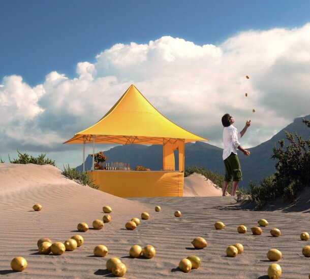 Yellow gazebo of the size 3x3 m with awning and various sidewalls on a sandy ground in the middle of the desert. A man is juggling next to the gazebo.  
